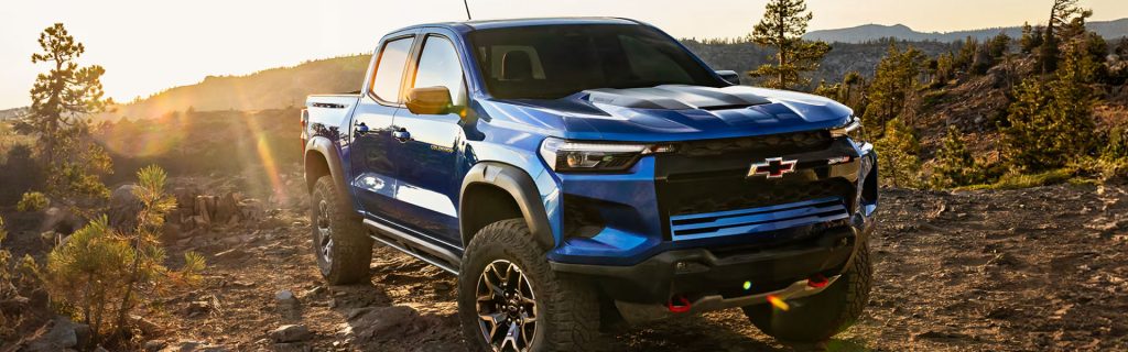 Blue Chevrolet pickup truck driving off-road on a rocky trail at sunset.