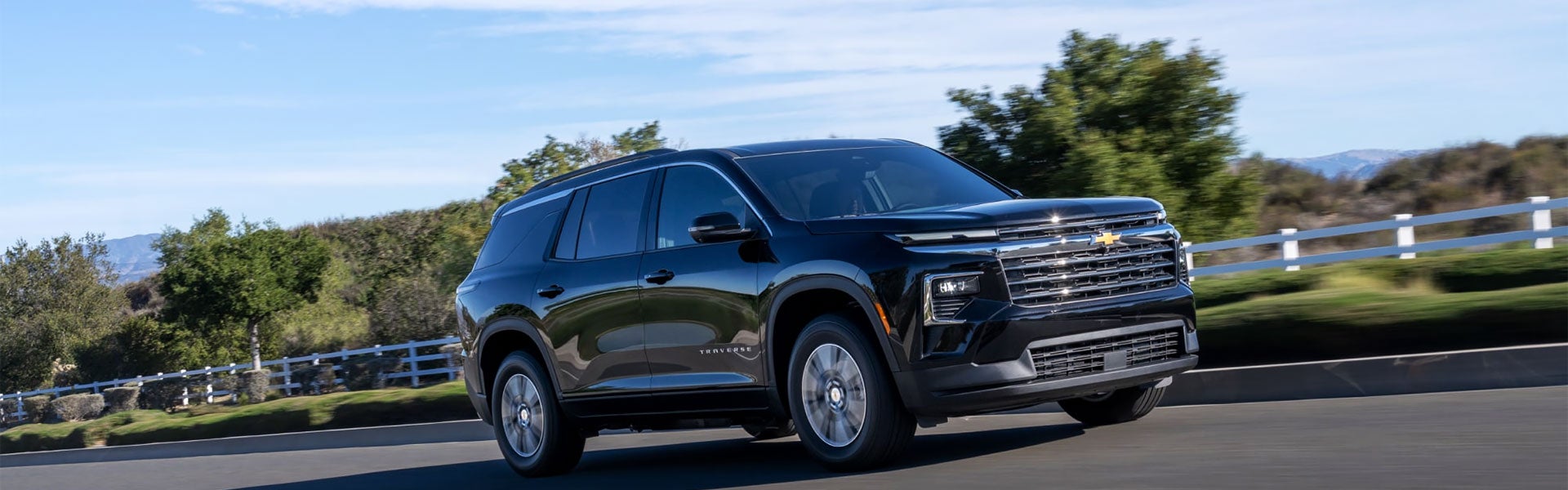 Black Chevrolet Traverse SUV driving on a road.